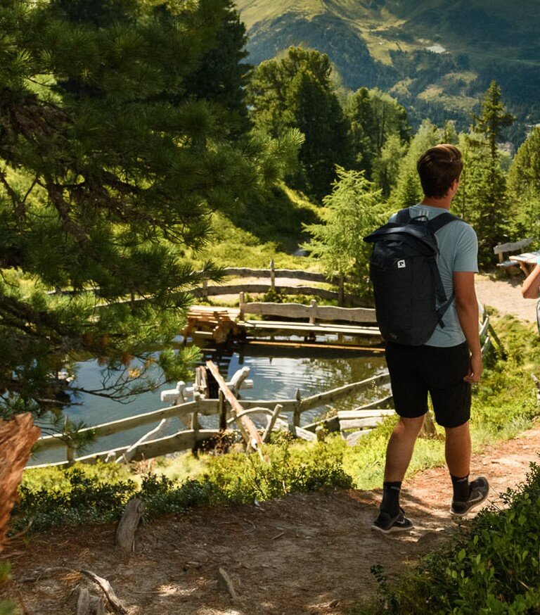 Two hikers on forest trail overlooking small water channel with wooden fence at Graukogel in summer | © Gasteinertal Tourismus GmbH