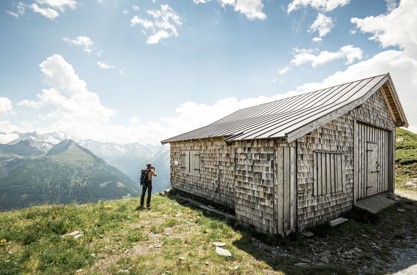 Hiker in front of rustic wooden hut at Stubnerkogel with view of lush alpine landscape and Hohe Tauern. | © Gasteiner Bergbahnen AG