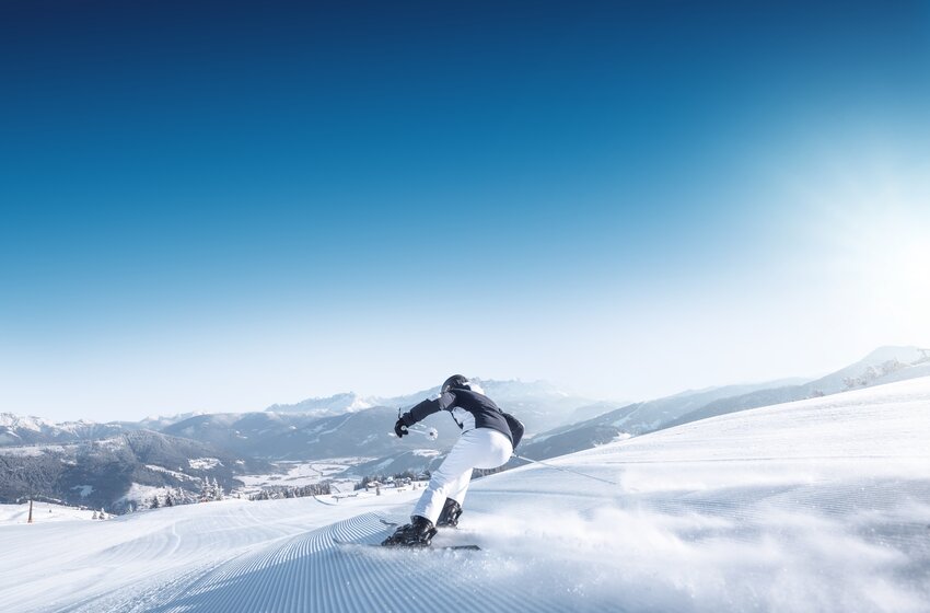 Skier cruising calmly on wide groomed slope with snowy alpine panorama in the background. | © Ski amadé GmbH