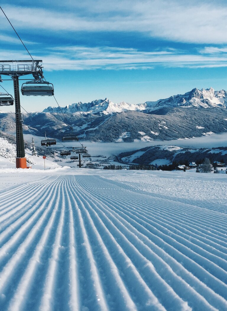 Chairlift above freshly groomed slope with snowy mountain and valley view. | © Ski amadé GmbH