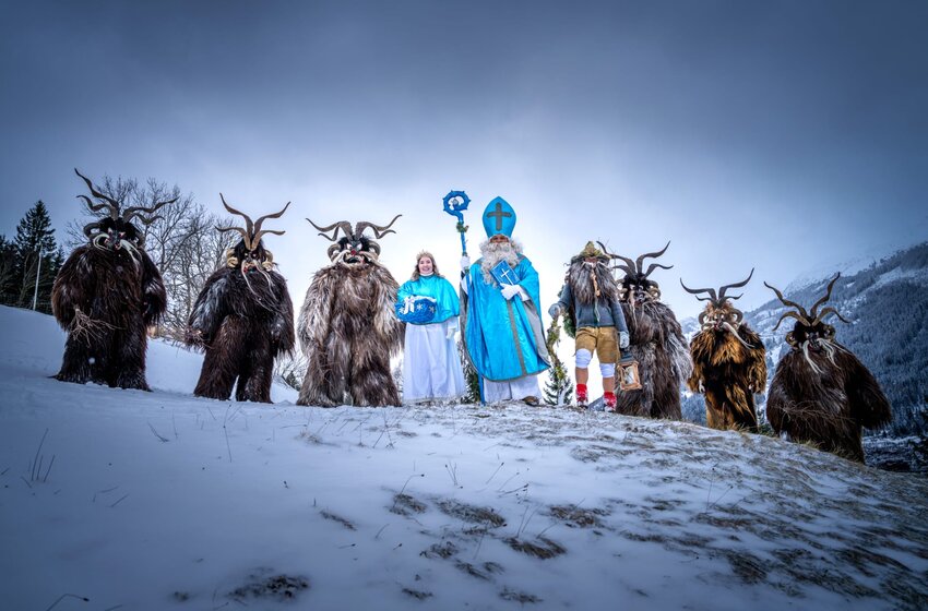 Krampusgruppe mit Nikolaus und Begleitern steht in Kostümen auf einem verschneiten Hang vor bewaldeten Bergen | © Gasteiner Bergbahnen AG 