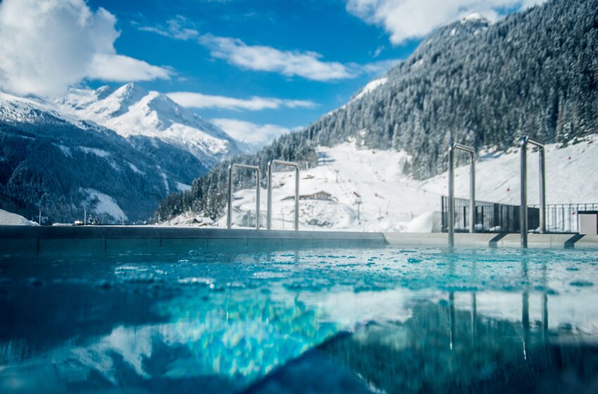 Beheizter Außenpool vor verschneiter Skipiste und bewaldeten Bergen unter blauem Himmel in Bad Gastein | © Max Steinbauer