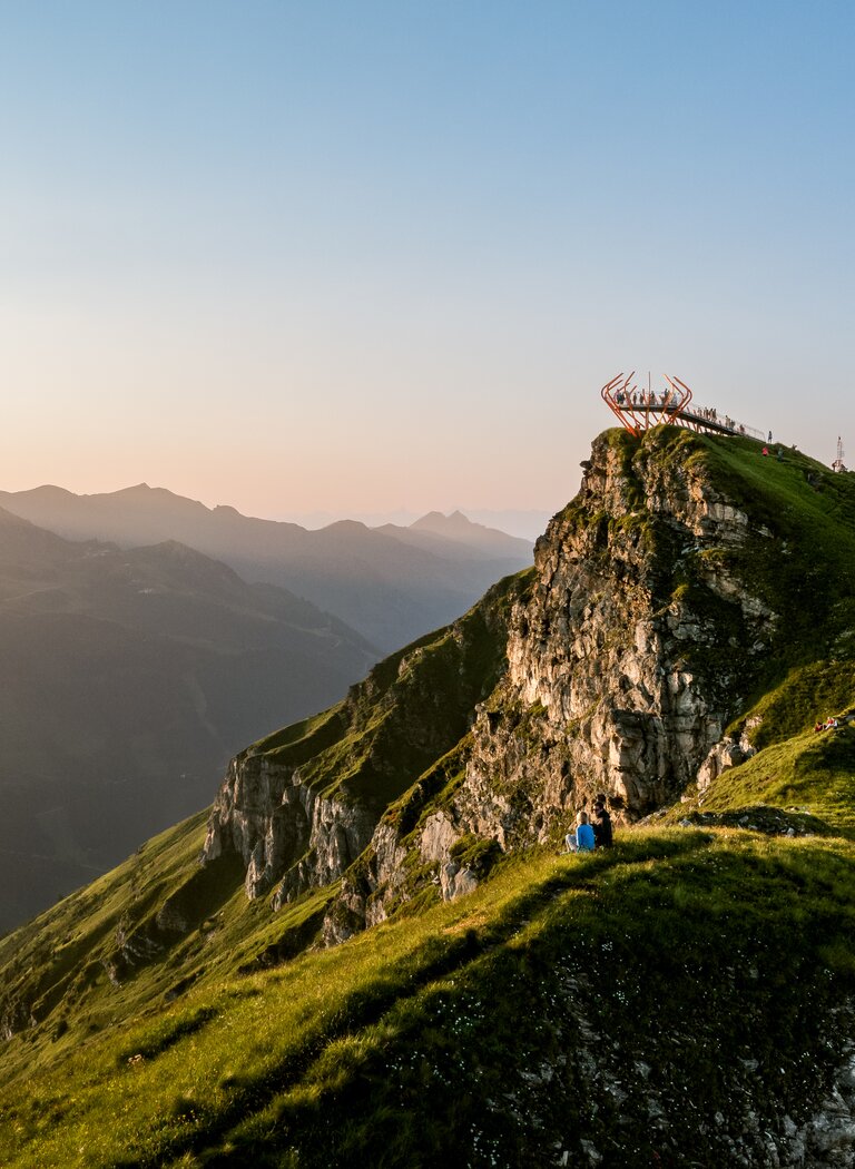 Aussichtsplattform auf felsigem Bergkamm mit Wanderweg, Hütte und Blick auf umliegende Berge im Abendlicht | © Gasteiner Bergbahnen AG