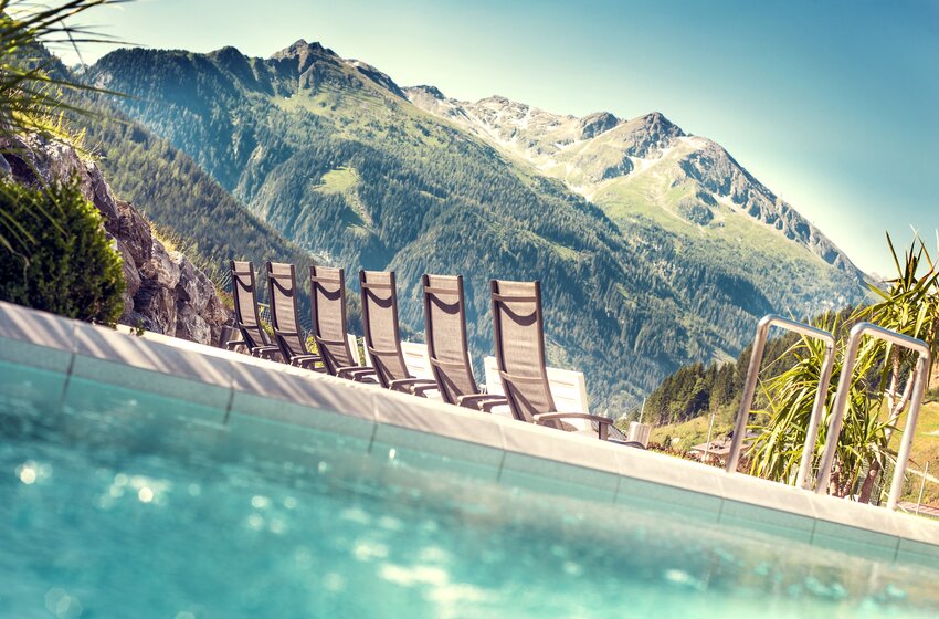 Mehrere Liegestühle stehen am Poolrand mit Blick auf grüne Berge und bewaldete Hänge unter klarem Himmel | © Max Steinbauer A 5640 Bad Gastein