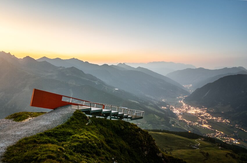 Moderne Aussichtsplattform auf Bergkante über beleuchtetem Tal mit Orten und Serpentinenstraße im Abendlicht | © Gasteiner Bergbahnen AG