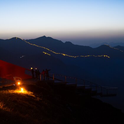 Aussichtsplattform mit Besuchern auf einem Berggipfel bei Dämmerung, Lichterkette entlang der Grate | © Gasteiner Bergbahnen AG