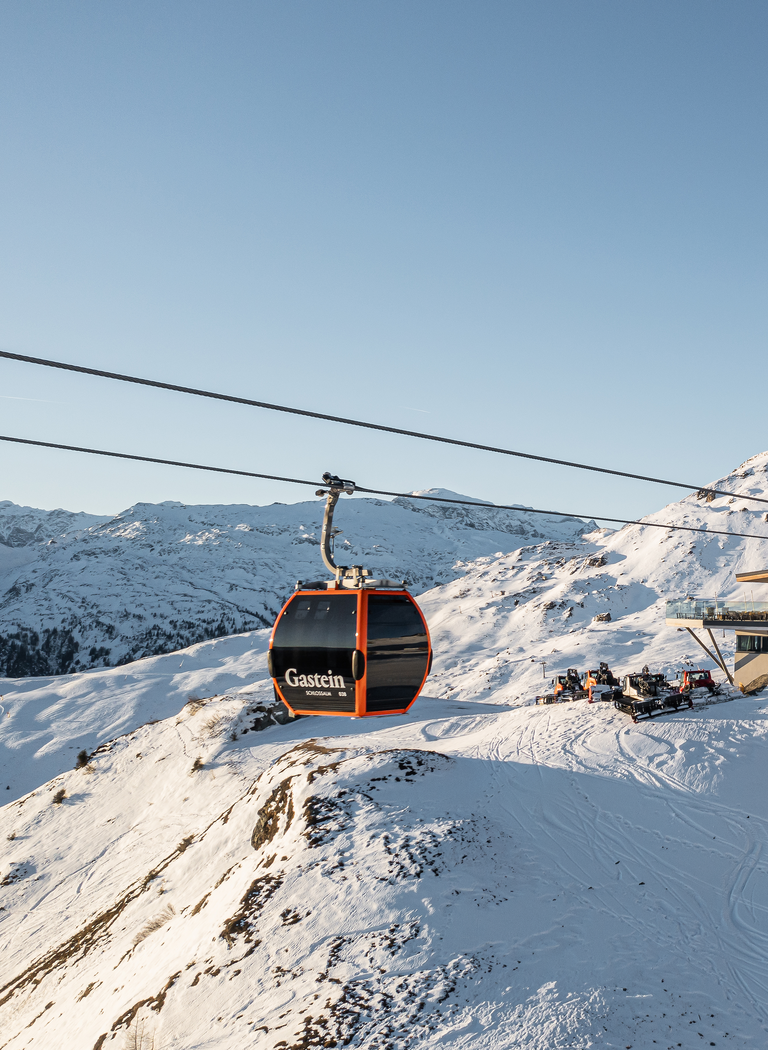 Orange Gondeln erreichen die Bergstation in einem verschneiten Skigebiet vor schroffen Alpen unter klarem Himmel. | © Gerhard Wolkersdorfer