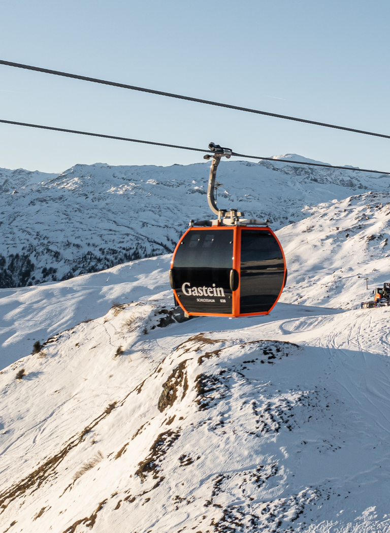 Orange Gondeln erreichen die Bergstation in einem verschneiten Skigebiet vor schroffen Alpen unter klarem Himmel. | © Gerhard Wolkersdorfer